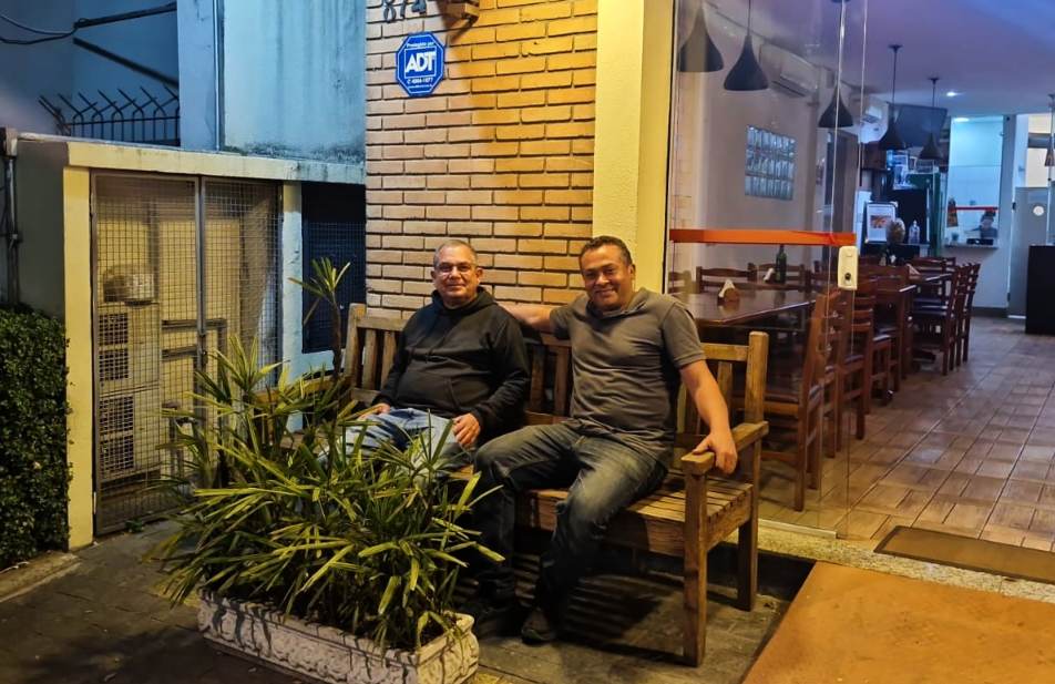 Homens sentados em banco rústico na entrada de restaurante à noite